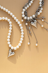 Elegant pearl and silver charm necklaces on beige background.  .Fashionable layered silver necklaces with pendants and with silver heart pendant