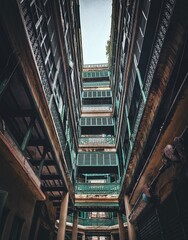 "Looking up at a historic building with ornate green balconies and shuttered windows, creating a striking perspective of aged elegance."

