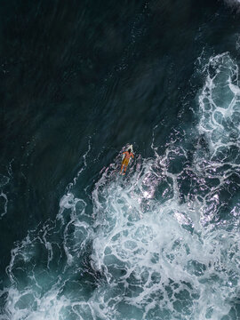 Aerial 90 degree straight down drone photo of a young male surfer on a surfboard in the white foamy ocean water. Pacific Coast, El Tunco beach town, El Salvador, Central America.	