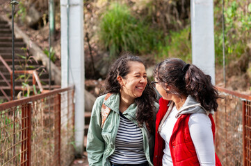 Fototapeta premium Two female tourists laughing and enjoying each other's company while walking across a suspension bridge