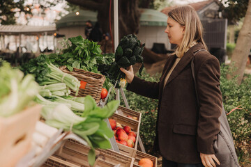 Middle-aged woman on the local Farmers market. Mature Female Customer Shopping At Farmers Market Stall. Beautiful woman buys a greens and vegetables. Close up. Part of the series.