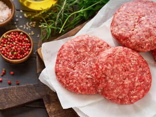 Four fresh raw burger patty or ground beef meat burger steak cutlets on dark wooden background. Top view.