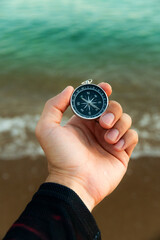 Pov of man hand holding navigational travel compass to find direction and next destination place. Concept of travel people and exploring. Beach and ocean in background