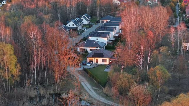 A residential enclave nestled among trees in the light of the setting sun, with houses and properties located on the outskirts of a large city, offering close contact with nature, aerial view.