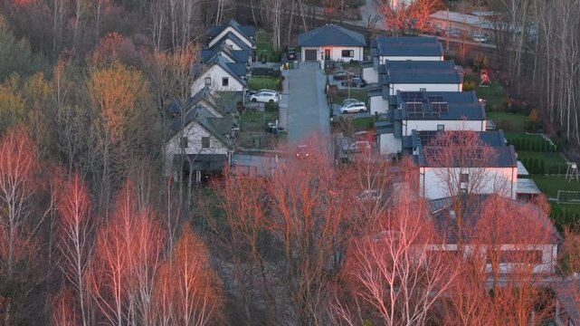 A residential enclave nestled among trees in the light of the setting sun, with houses and properties located on the outskirts of a large city, offering close contact with nature, aerial view.