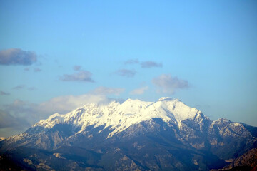 High impregnable mountains with large white snow caps on tops under blue sky with some clouds