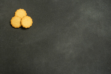 Three yellow cookies on dark textured moody background.