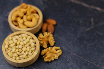 An appealing display of assorted nuts in wooden bowls against a dark stone background creates an inviting atmosphere