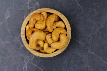 A closeup view showcasing roasted cashew nuts beautifully arranged in a round wooden bowl on a dark surface