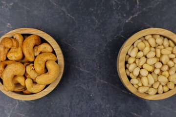 Two wooden bowls filled with crunchy cashews and delicious almonds resting on a dark marble surface