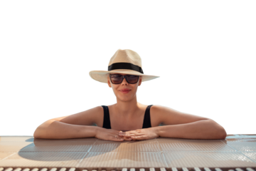 Girl in hat is in pool, leaning on side. Young woman with glasses and hat on vacation is relaxing on edge of pool on sunny day. Portrait of woman in pool looking at camera. Sitting on edge of pool