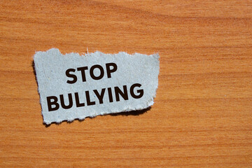 Stop bullying message written on ripped torn grey paper piece on wooden background. Conceptual stop...