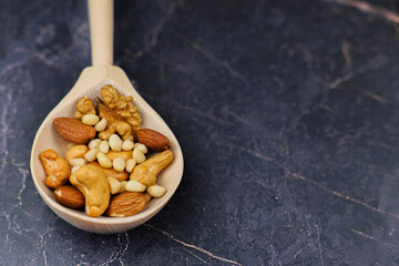 A beautiful closeup image of mixed nuts beautifully arranged in a wooden spoon set against a dark marble surface