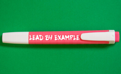 Lead by example message written on pink marker pen on green background. Conceptual lead by example...