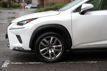 Close-up of a white SUV’s wheel and fender on a rainy urban street, highlighting modern...