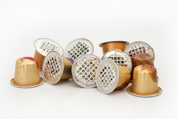Used coffee capsules in various metallic colors scattered on a white background.