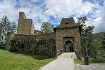 Entrance to Velhartice Castle with stone walls, gate, and bridge under a blue sky with white clouds. Historic medieval ruin in the Czech Republic.






