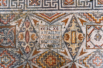 Intricate Byzantine mosaic featuring geometric patterns and a central Greek inscription on a floor of ruined ancient church in Hurvat Beit Loya, Israel