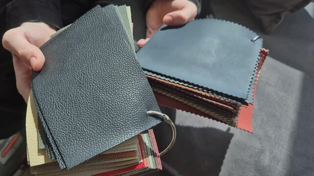 A man holds samples of genuine leather for upholstery of a car interior