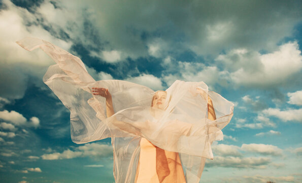 Ethereal figure enveloped in flowing fabric under cloudy sky
