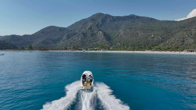 Aerial footage of a speedboat going towards green mountain on a sunny day with blue sky