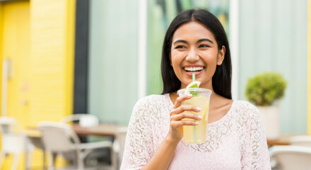 Fototapeta premium Smiling young asian female enjoying refreshing lemonade outdoors