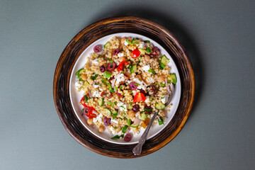 Vibrant couscous salad served on a white plate, resting on a natural wicker charger against a solid background. 