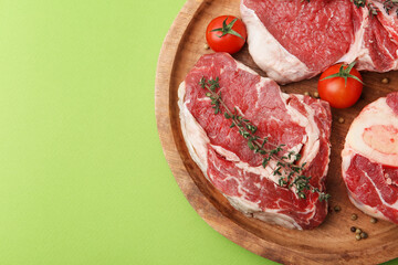 Pieces of raw beef, spices and tomatoes on green table, top view. Space for text