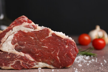 One piece of raw beef with salt on brown textured table against black background, closeup