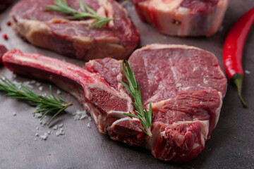 Pieces of raw beef, rosemary and salt on brown textured table, closeup