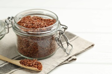 Raw brown rice in open jar and spoon on white wooden table, closeup. Space for text