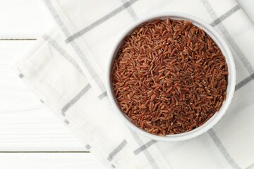 Raw brown rice in bowl on white wooden table, top view. Space for text