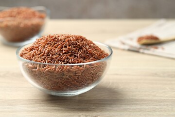 Brown rice in glass bowl on wooden table, closeup. Space for text