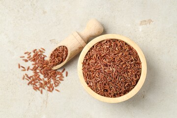 Brown rice in bowl and scoop on light grey table, flat lay