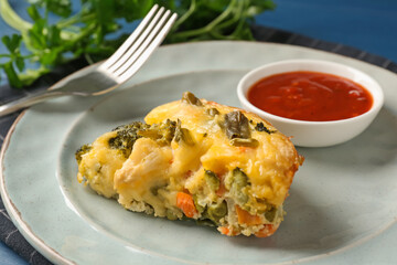 Piece of tasty vegetable casserole and sauce on blue table, closeup