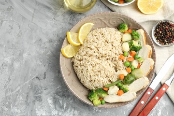 Delicious brown rice with chicken, vegetables and lemon slices served on grey textured table, flat lay. Space for text