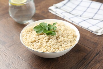 Delicious brown rice with parsley served on wooden table, closeup