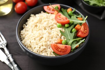 Delicious brown rice with vegetables on black wooden table, closeup