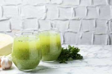 Healthy parsley smoothie in glasses, garlic and leaves on white marble table against grey textured background, closeup. Space for text