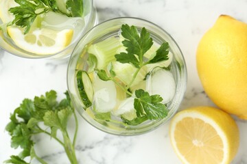 Healthy drink with parsley, cucumbers, lemons and celery on white marble table, flat lay