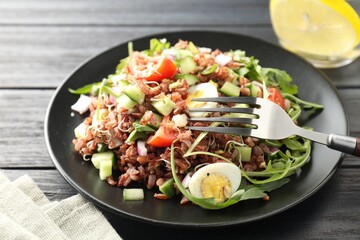 Delicious salad with brown rice on black wooden table, closeup