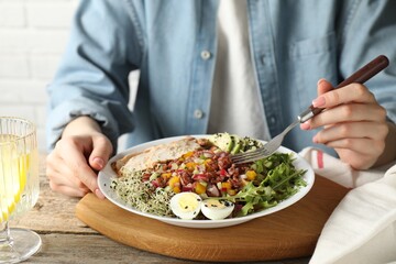 Woman eating delicious salad with brown rice at wooden table, closeup