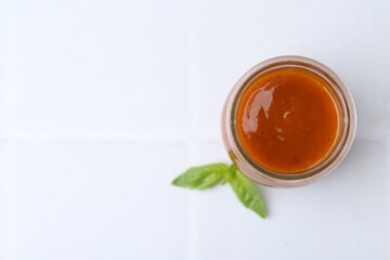 Tasty curry sauce in glass jar and basil on table, top view. Space for text