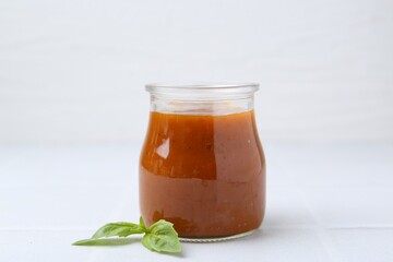 Tasty curry sauce in glass jar and basil on white tiled table, closeup