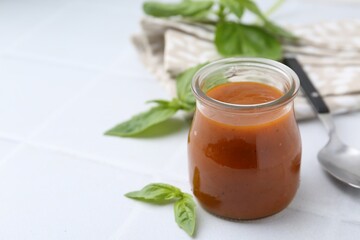 Tasty curry sauce in glass jar and basil on white tiled table, closeup. Space for text