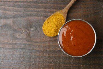 Tasty curry sauce in metal dish and powder on wooden table, top view. Space for text