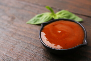 Tasty curry sauce and basil leaves on wooden table, closeup. Space for text