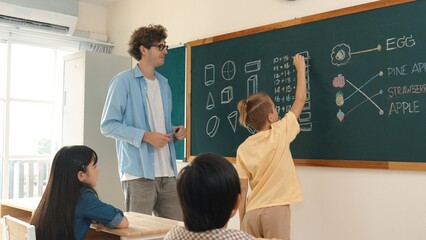 Smart boy writing answer of math theory while standing at blackboard. Attractive male teacher...