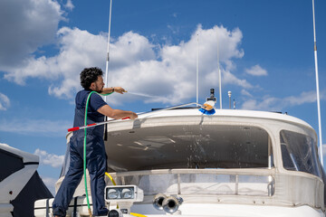 Boat maintenance worker providing cleaning service on a moored yacht. Maritime professional washing...