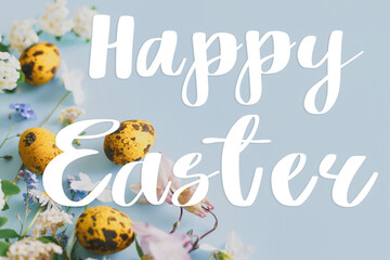Happy Easter! Greeting card with Happy Easter text, easter eggs and spring flowers flat lay on blue background